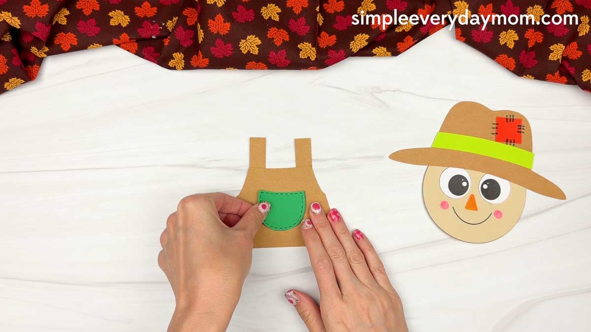 Hands gluing the overall pocket onto the center of the overalls for the Fork Painted Scarecrow Craft.