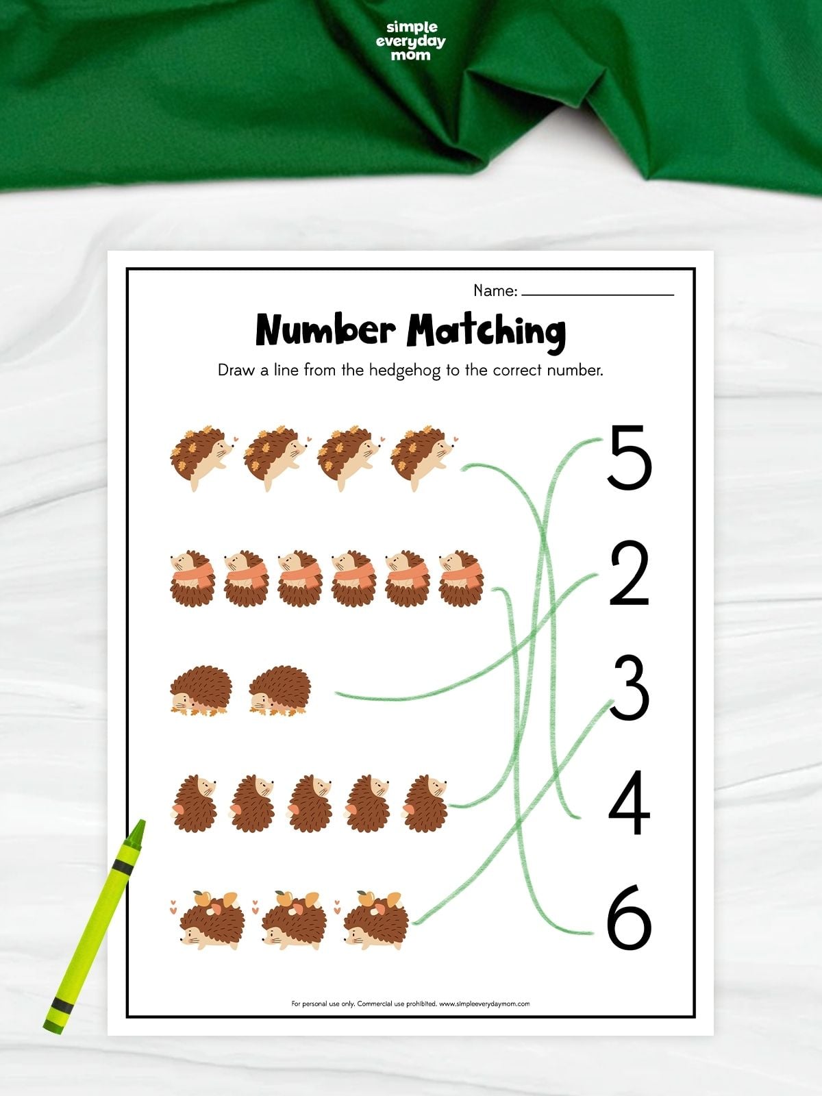 A hedgehog number matching worksheet with groups of two to six hedgehogs and numbers to match. Children count each group and draw a line to the correct number. A green crayon rests beside the completed worksheet.