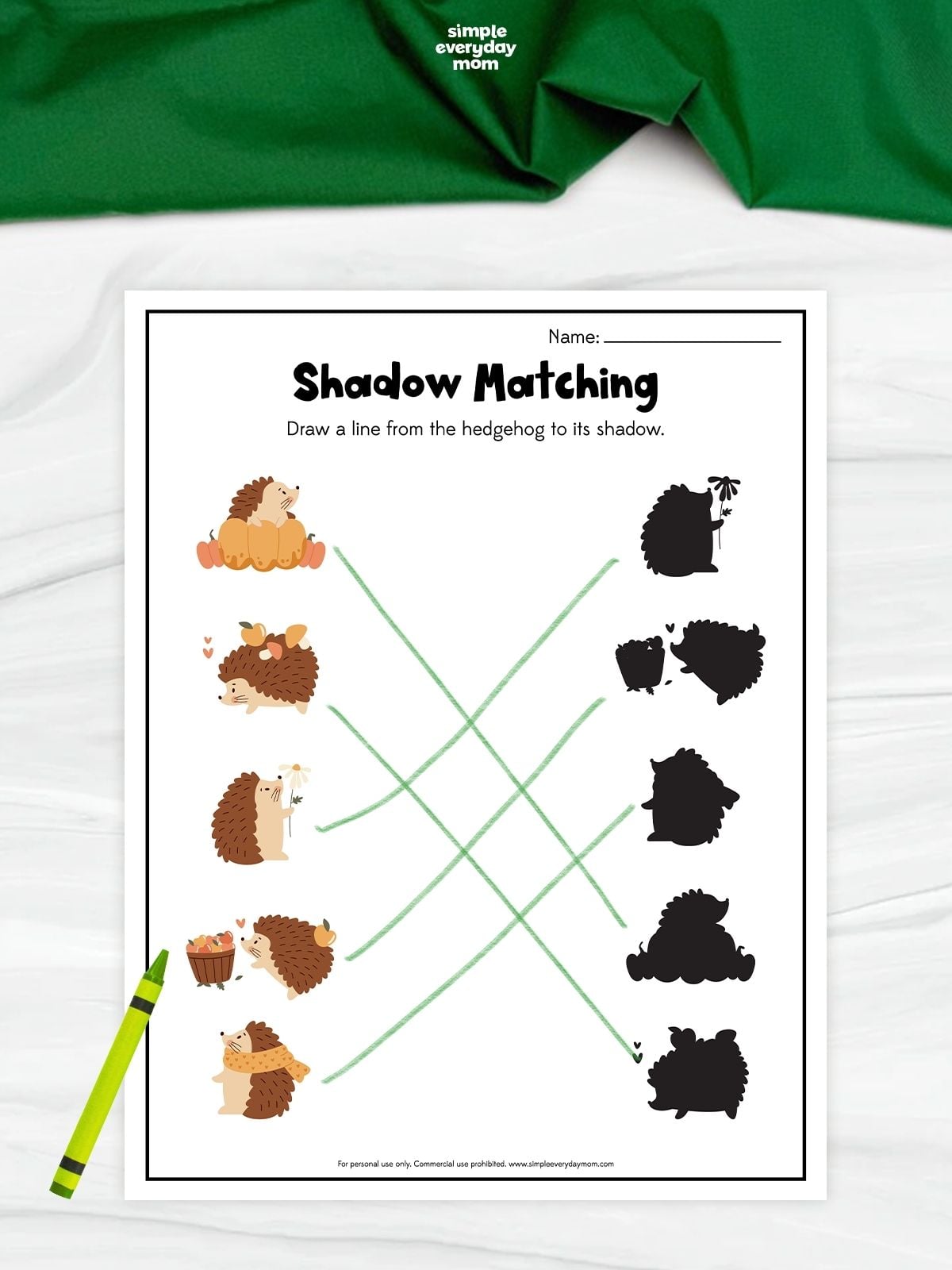 A hedgehog shadow matching worksheet with five fall-themed hedgehog illustrations and their silhouettes. Children draw lines to connect each hedgehog with its matching shadow. A green crayon rests beside the completed worksheet.