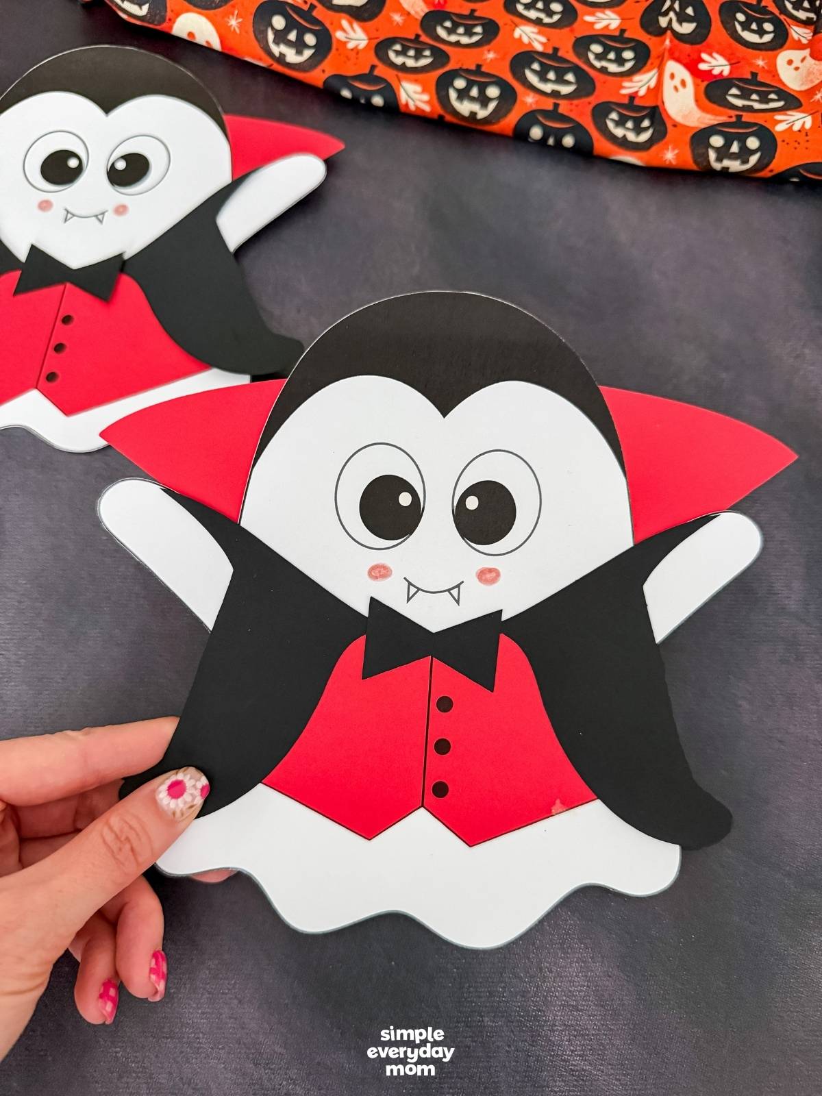 Hands holding the completed Vampire Ghost Disguise Craft featuring a cape, collar, bow tie, and vampire vest.