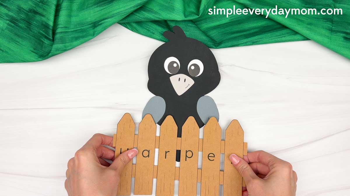 Hands holding the personalized name fence in front of the completed crow craft.