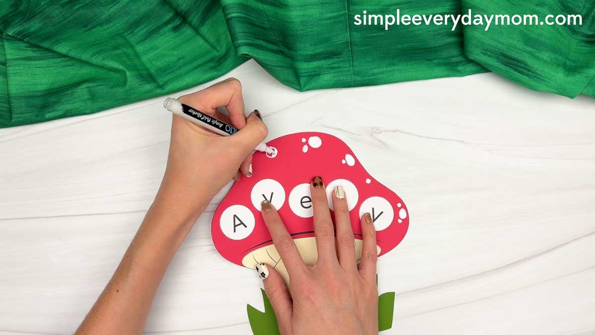 Hands using a white marker to add decorative spots to the red mushroom cap with the name Avery.