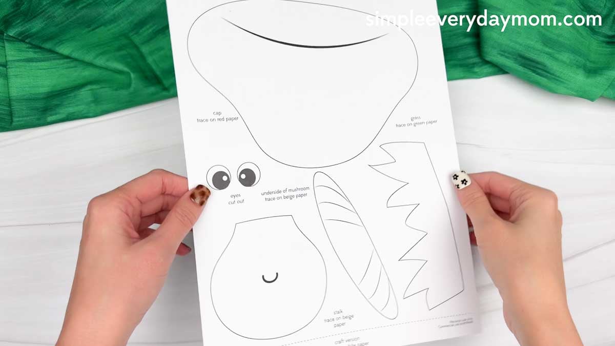 Hands holding a printable mushroom name craft template with cap, grass, eyes, and body pieces.