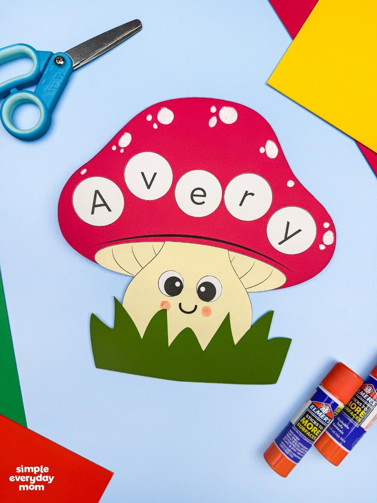 A completed Craft featuring a smiling mushroom name craft spelling Avery, surrounded by scissors, glue sticks, and colorful paper.