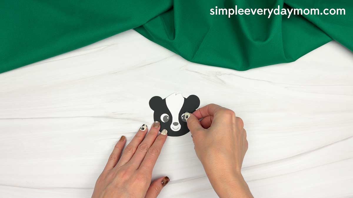 hands attaching an eye piece to the black and white skunk face cutout.