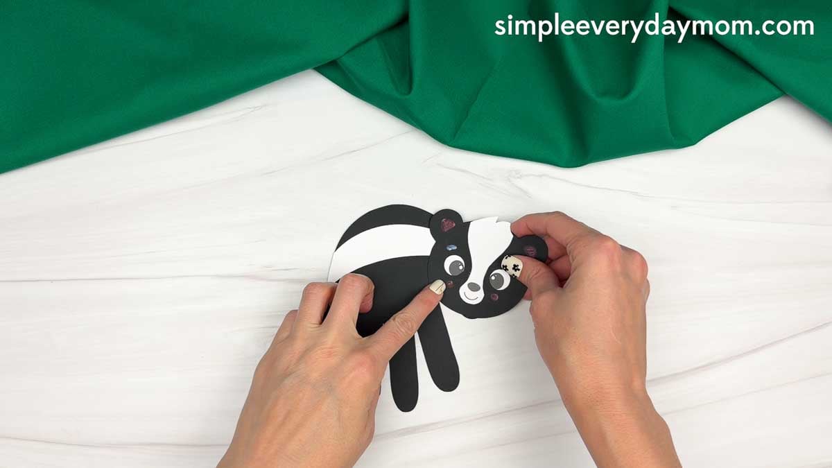 hands attaching the skunk head to the black handprint body with a white stripe.