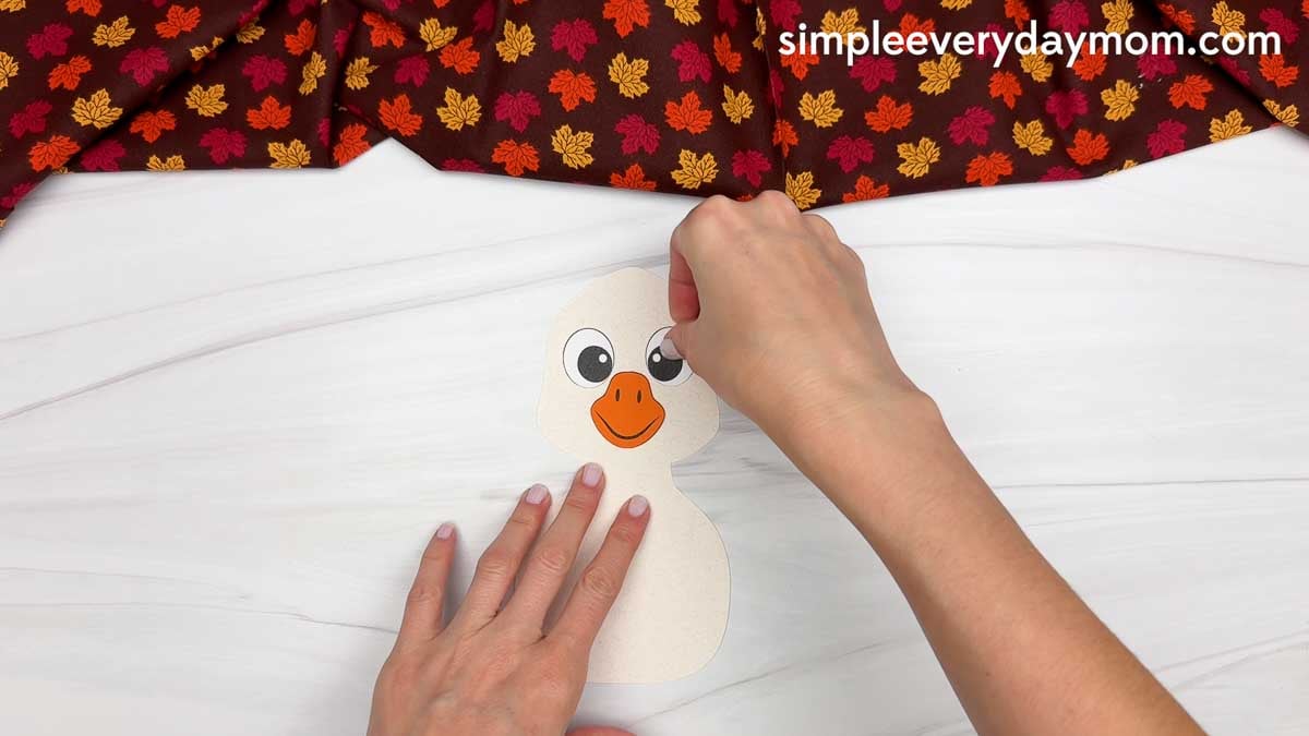Hands gluing the eyes above the orange beak on the white goose for a Thankful Goose Craft.