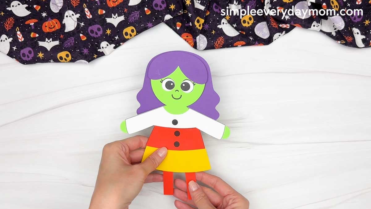 Hands attaching the witch’s legs underneath the candy corn dress.