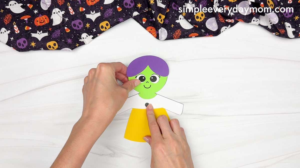 Hands assembling the candy corn colored dress onto the witch’s body.