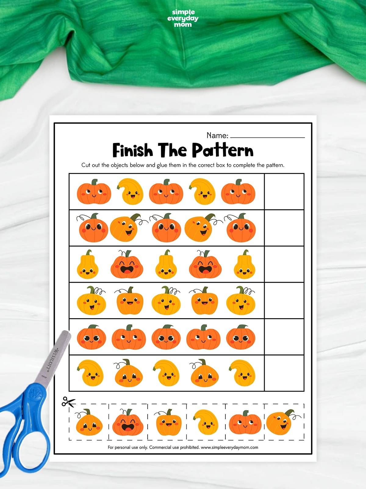 A completed pumpkin pattern worksheet features rows of cheerful orange and yellow pumpkins and gourds arranged in repeating sequences. Kids cut out the pumpkin pictures at the bottom and glue the correct one into each empty box to finish the patterns. Blue scissors sit beside the printable on a white surface with green fabric above.