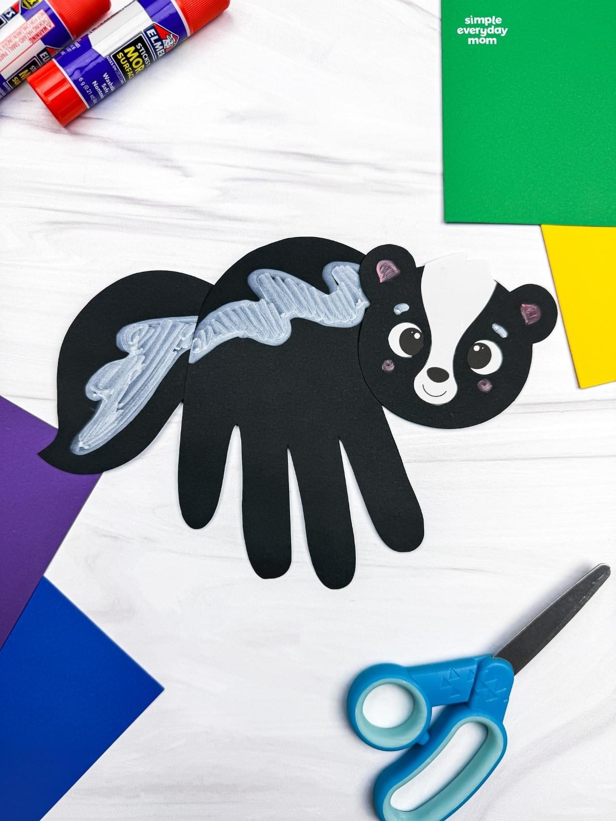 A completed Craft featuring a black handprint skunk with silver stripes surrounded by colorful craft supplies.
