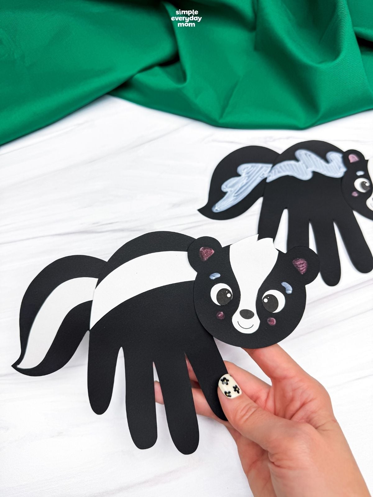 hands holding a completed black handprint skunk craft with white stripes.