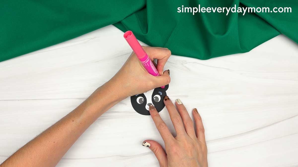 hands using a pink marker to add color to the skunk face cutout.