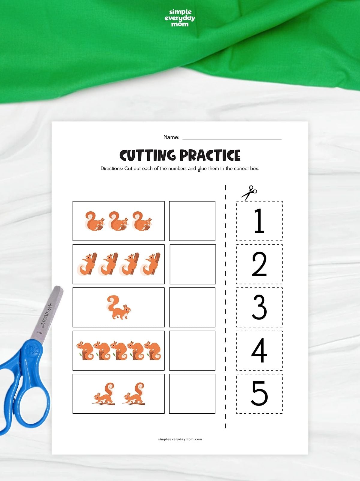 A squirrel-themed cutting practice worksheet with groups of one to five squirrels and matching number cutouts. Children count the squirrels, cut out the numbers, and glue each number into the correct box. Blue scissors sit beside the printable on a white surface with green fabric above.