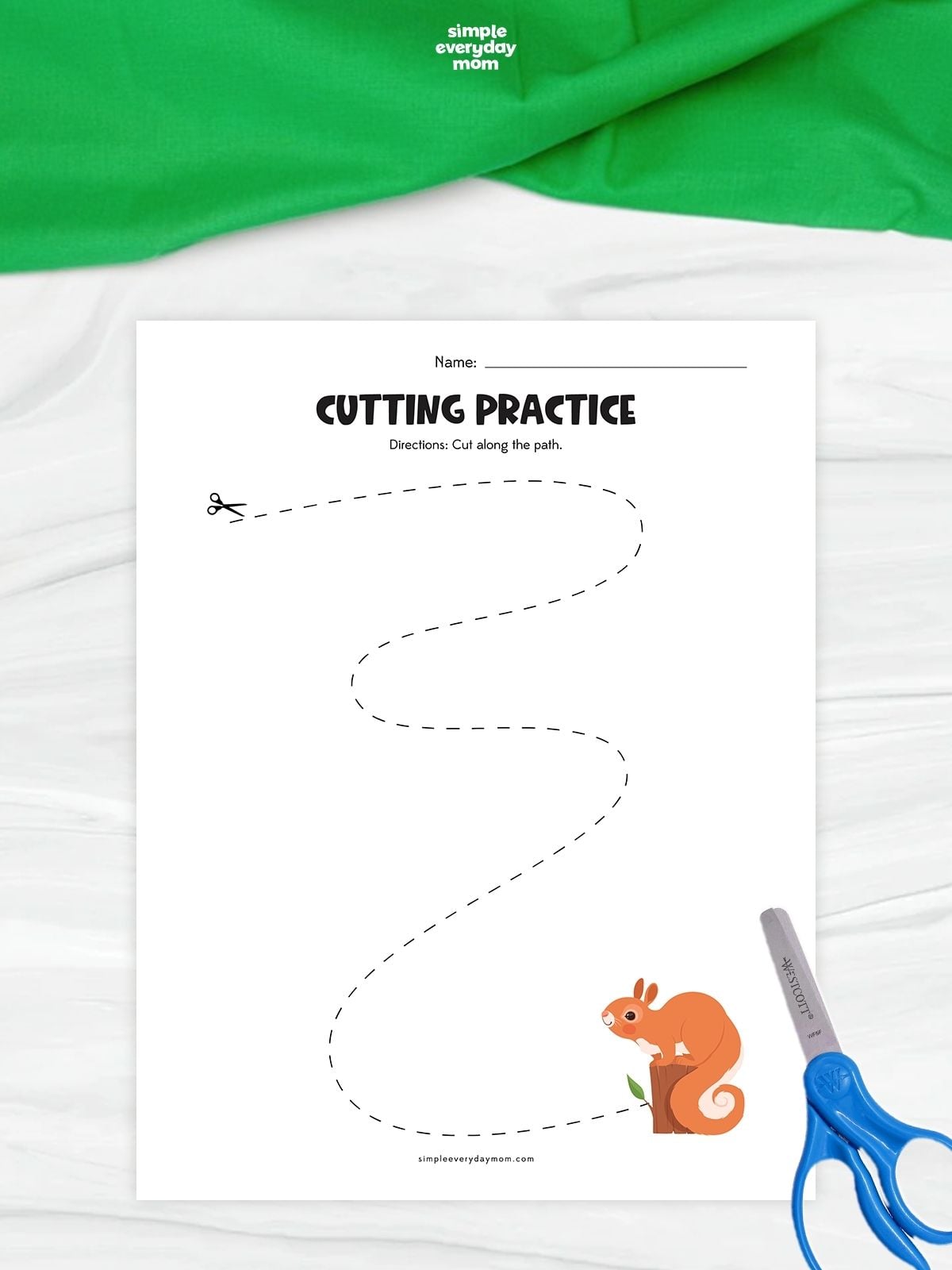 A squirrel cutting practice worksheet with a long curved dashed path leading to an orange squirrel. Children follow the winding line with scissors to practice cutting and fine motor skills. Blue scissors rest beside the printable on a white surface with green fabric above.