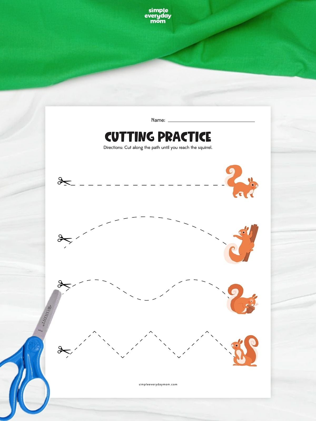 A squirrel cutting practice worksheet with four dashed paths leading to illustrated squirrels. Children practice scissor skills by cutting along straight, curved, wavy, and zigzag lines. Blue scissors rest beside the printable on a white surface with green fabric above.