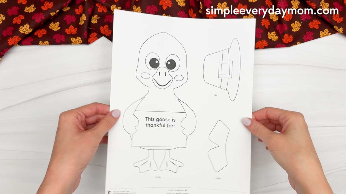 Hands holding a printable Thankful Goose Craft template featuring a goose, pilgrim hat, collar, and thankful message.