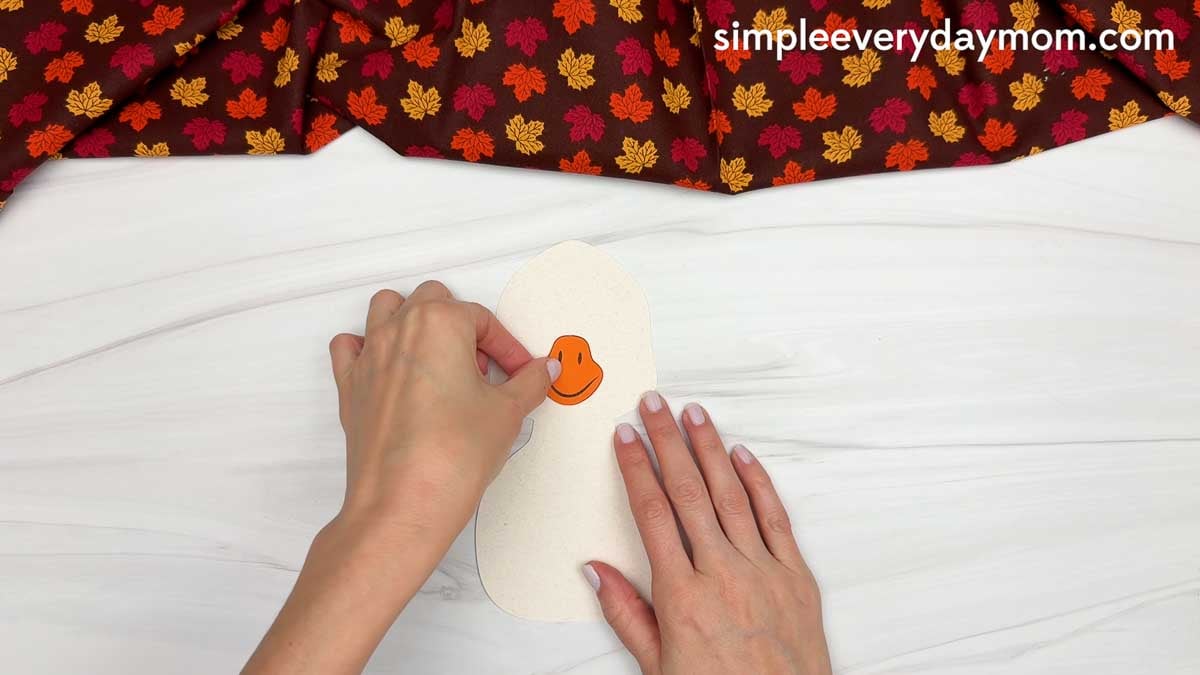 Hands gluing an orange beak onto the white goose head for a Thankful Goose Craft.