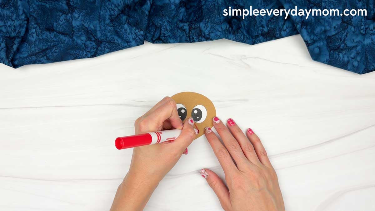 hands using a red marker to add details to the chef turkey disguise craft face.