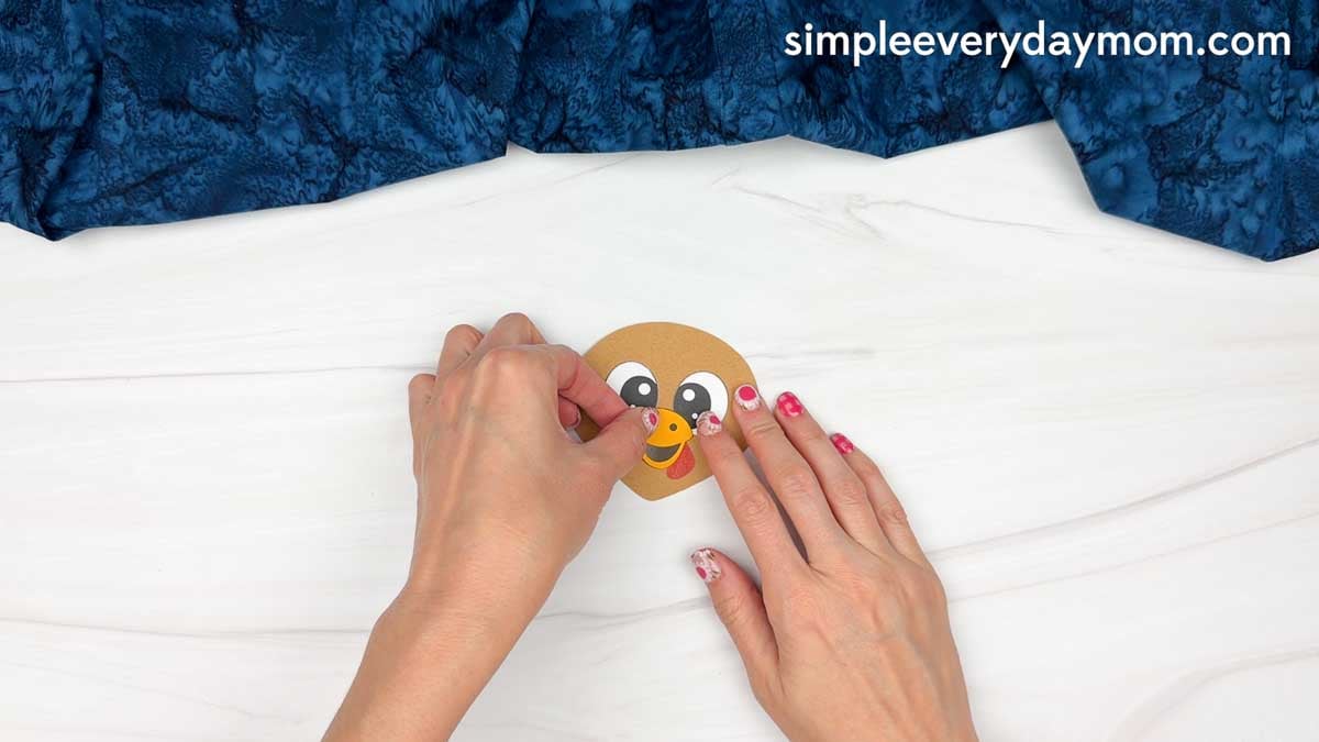 hands placing a yellow beak onto the chef turkey disguise craft face.