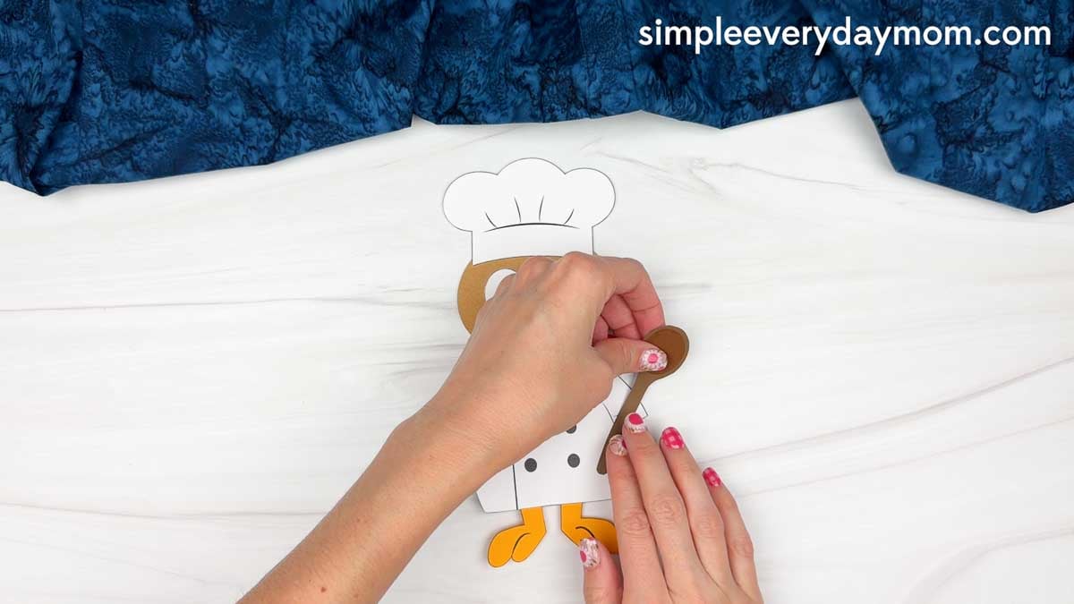 hands attaching a brown spoon to the chef turkey disguise craft.