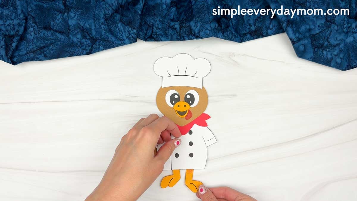 hands attaching orange feet to the chef turkey disguise craft.