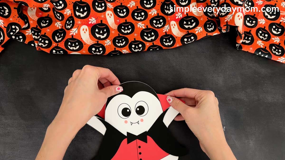 Hands gluing the vampire collar behind the top of the ghost head for the Vampire Ghost Disguise Craft.