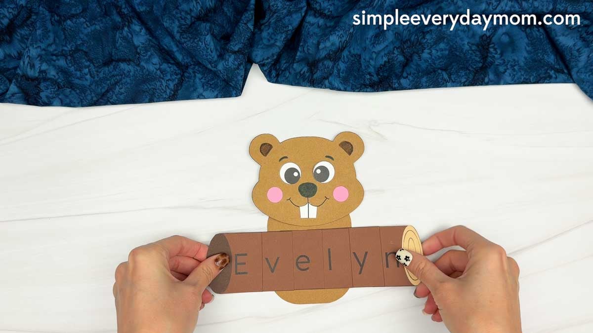 Hands holding the finished name log in front of the beaver for the Beaver Name Craft.