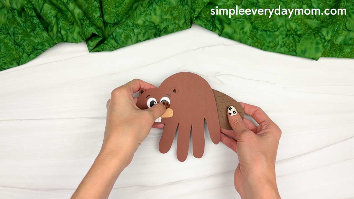 Hands attaching the tail behind the handprint beaver body.