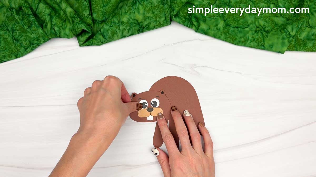Hands attaching the beaver head to the handprint for the Beaver Handprint Craft.