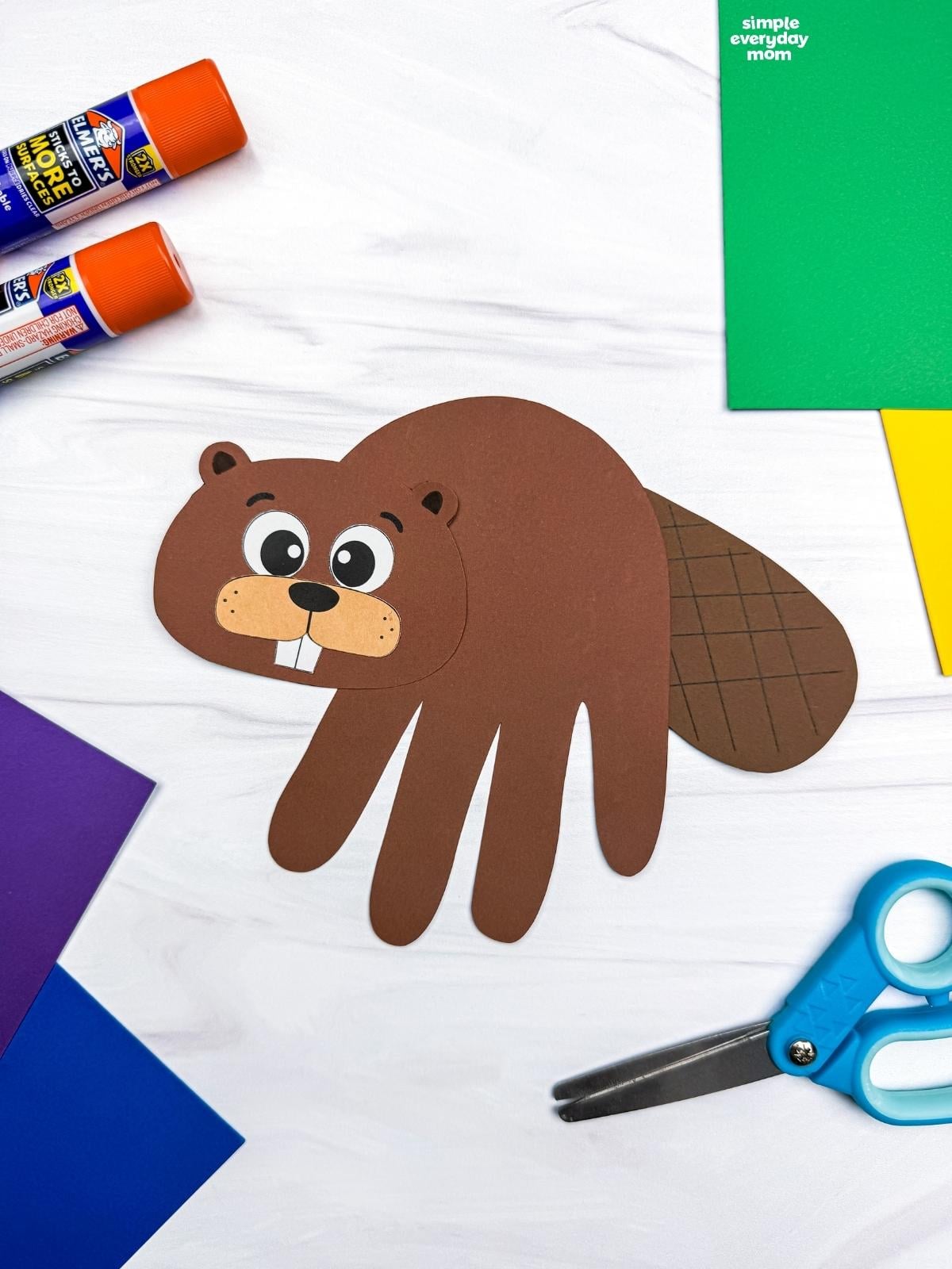 A completed Beaver Handprint Craft displayed with paper, scissors, and glue sticks.