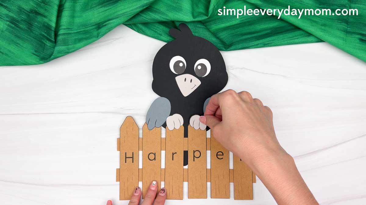 Hands gluing the crow’s feet over the top of the personalized name fence.