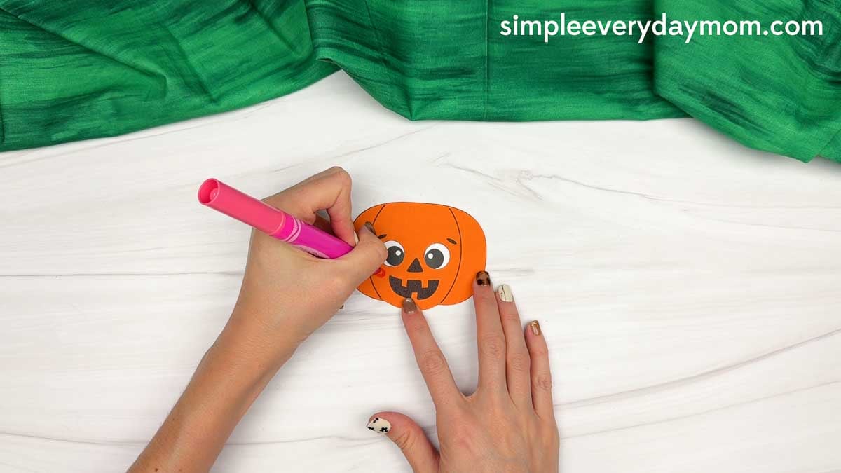 Hands drawing details on the face of a pumpkin for a Pumpkin Head Scarecrow Craft.