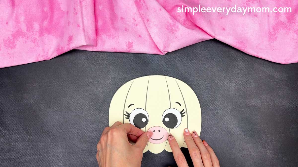 Hands gluing the smiling muzzle onto the center of the unicorn pumpkin craft.
