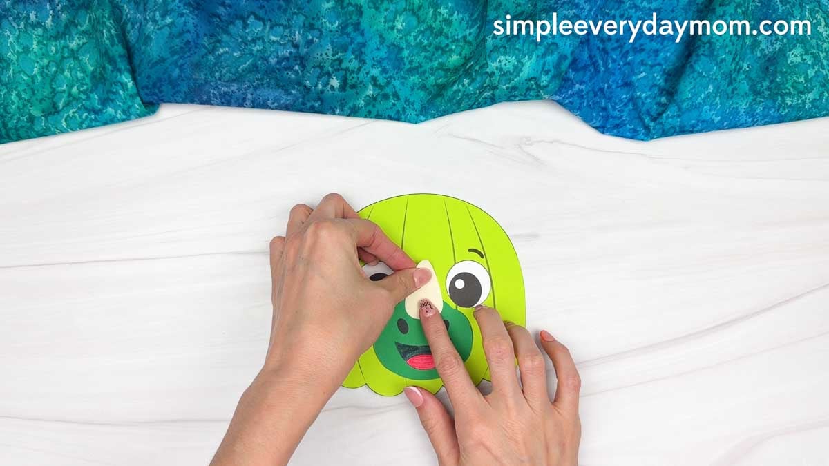 Hands gluing the nose horn above the snout of the dinosaur pumpkin craft.