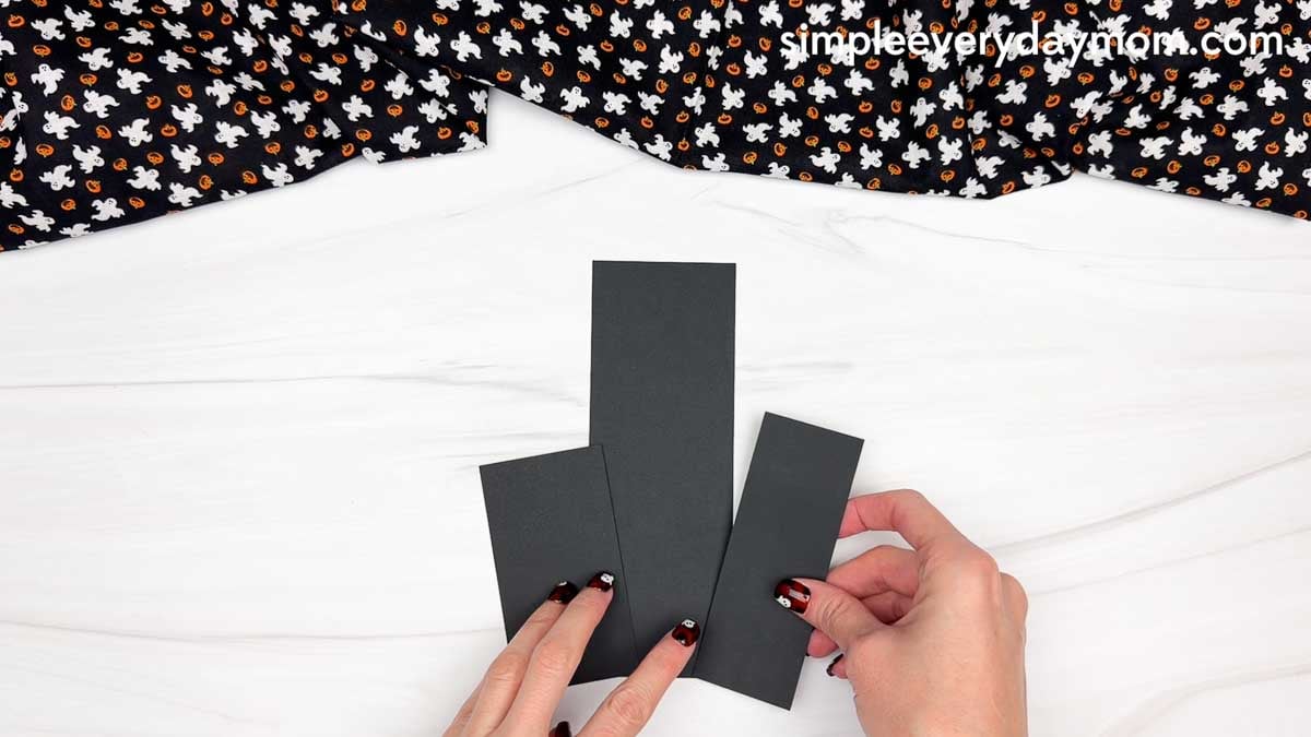 Hands arranging rectangular paper pieces to form the base of a haunted house shape craft.