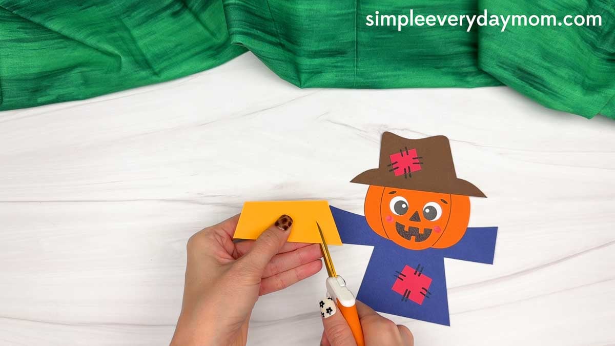 Hands cutting fringe into a paper straw piece for the scarecrow craft.
