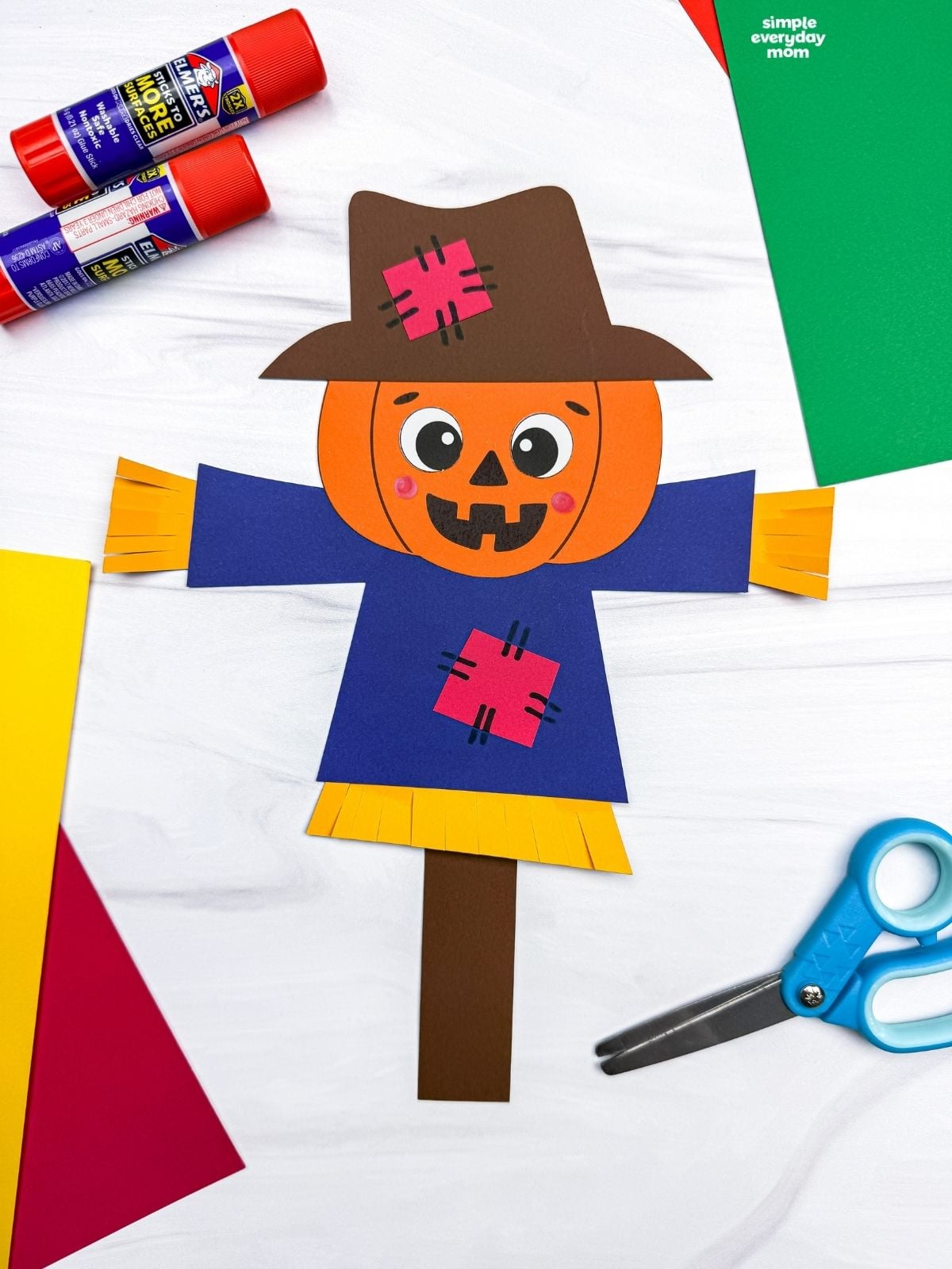 A completed Craft showing a pumpkin head scarecrow with a patched hat, shirt, straw details, and paper stick.