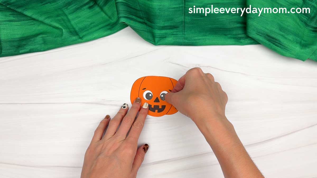 Hands attaching an eye to the pumpkin head for the scarecrow craft.