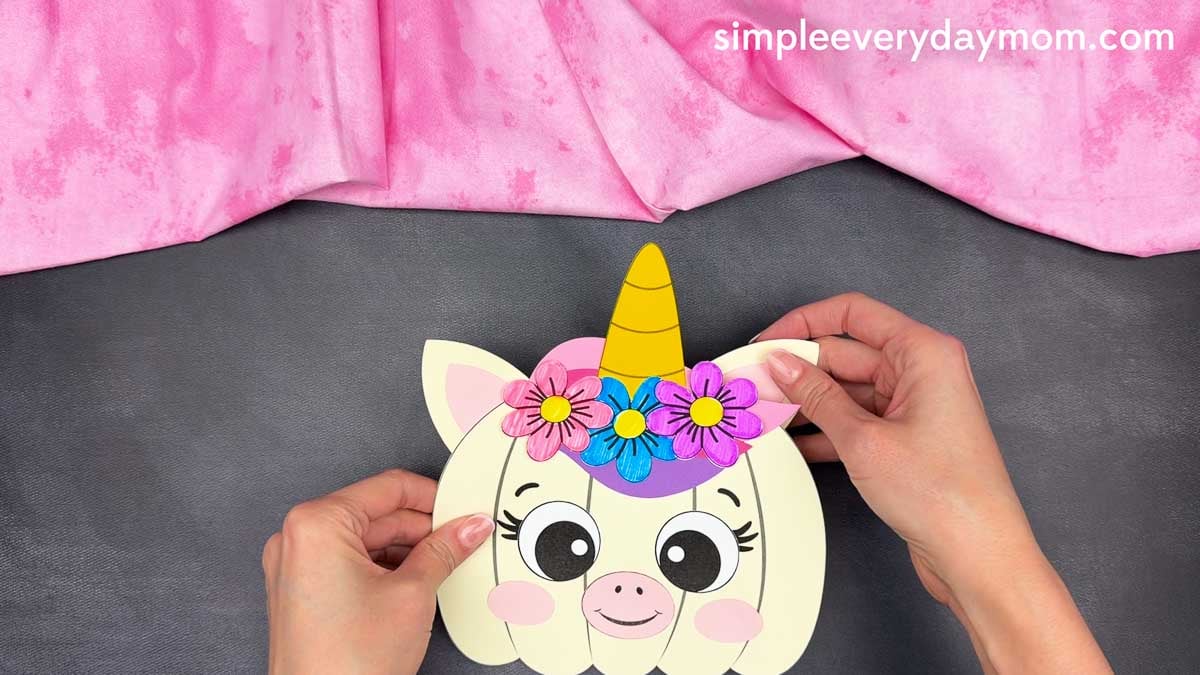 Hands gluing the ears behind the top of the unicorn pumpkin craft.