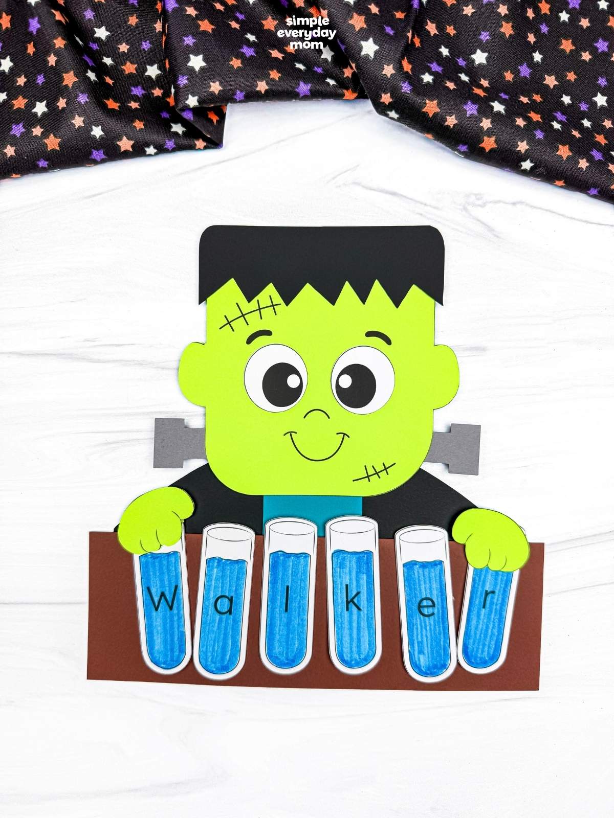 A completed craft showing a Frankenstein holding blue lettered test tubes that spell a child’s name.