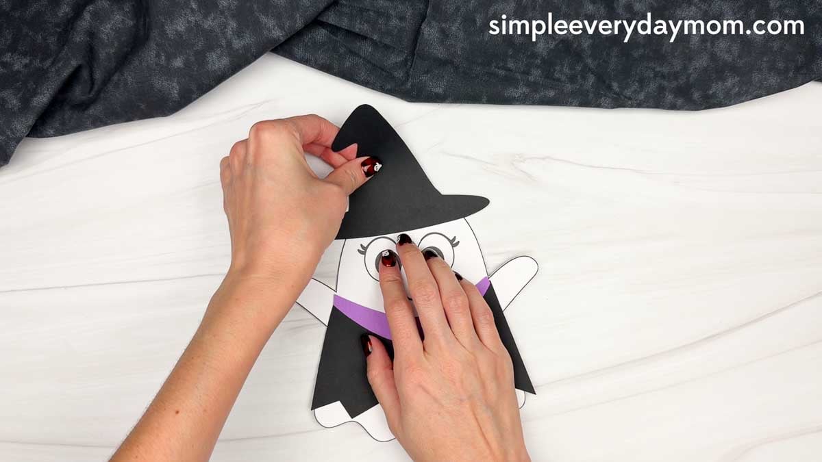 Hands placing the witch hat on top of the ghost’s head for a Witch Ghost Disguise craft.