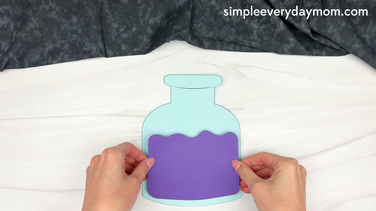 Hands placing the potion liquid piece onto a Halloween potion bottle craft.