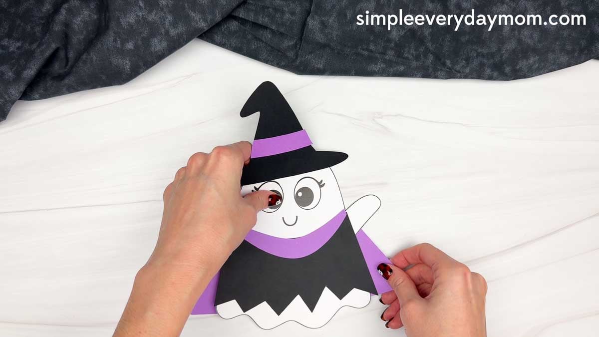 Hands attaching the witch sleeves over the ghost’s arms to complete the disguise.