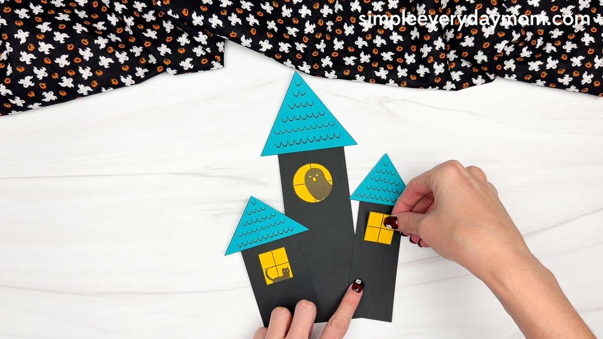 Hands adding a square window to the right side of the haunted house shape craft.