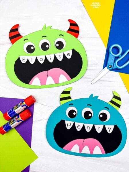 Side by side completed monster name crafts with three eyes, striped horns, and personalized letter teeth.