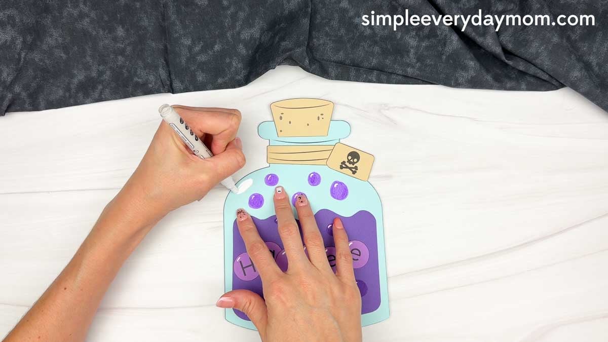 Hands using a white marker to add highlights to the bubbles on the Halloween potion bottle craft.