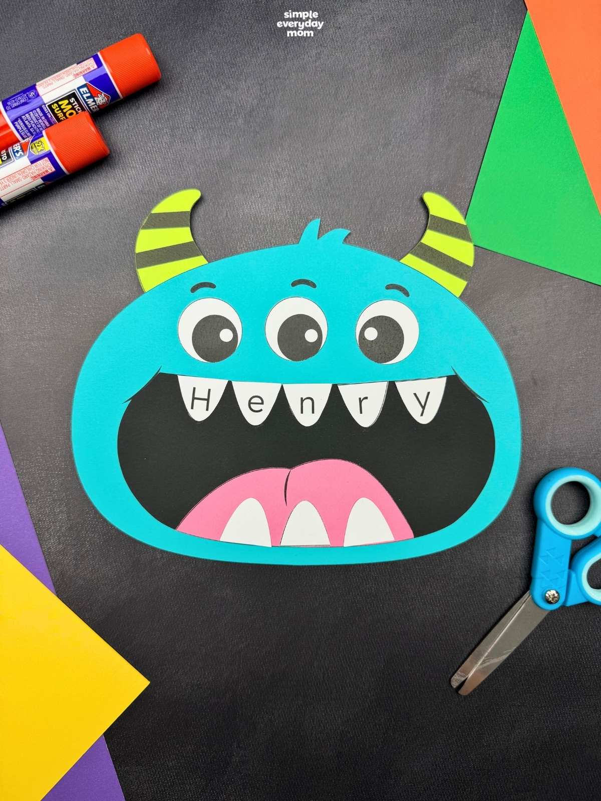 A completed craft featuring a blue monster with three eyes, striped horns, and the name Henry written across its teeth.