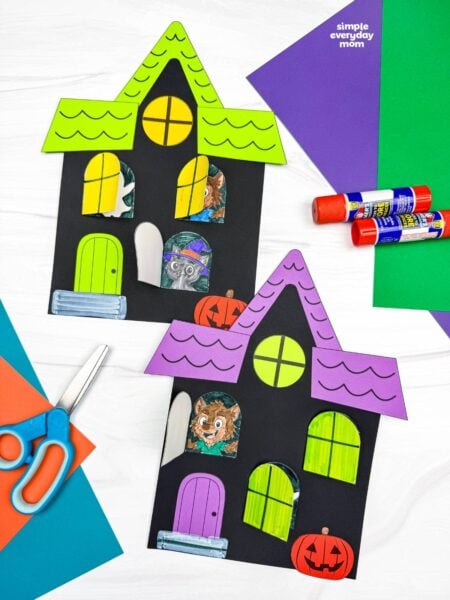 A completed craft display featuring two Peekaboo Haunted House Crafts with opening windows, Halloween characters, pumpkins, and craft supplies.