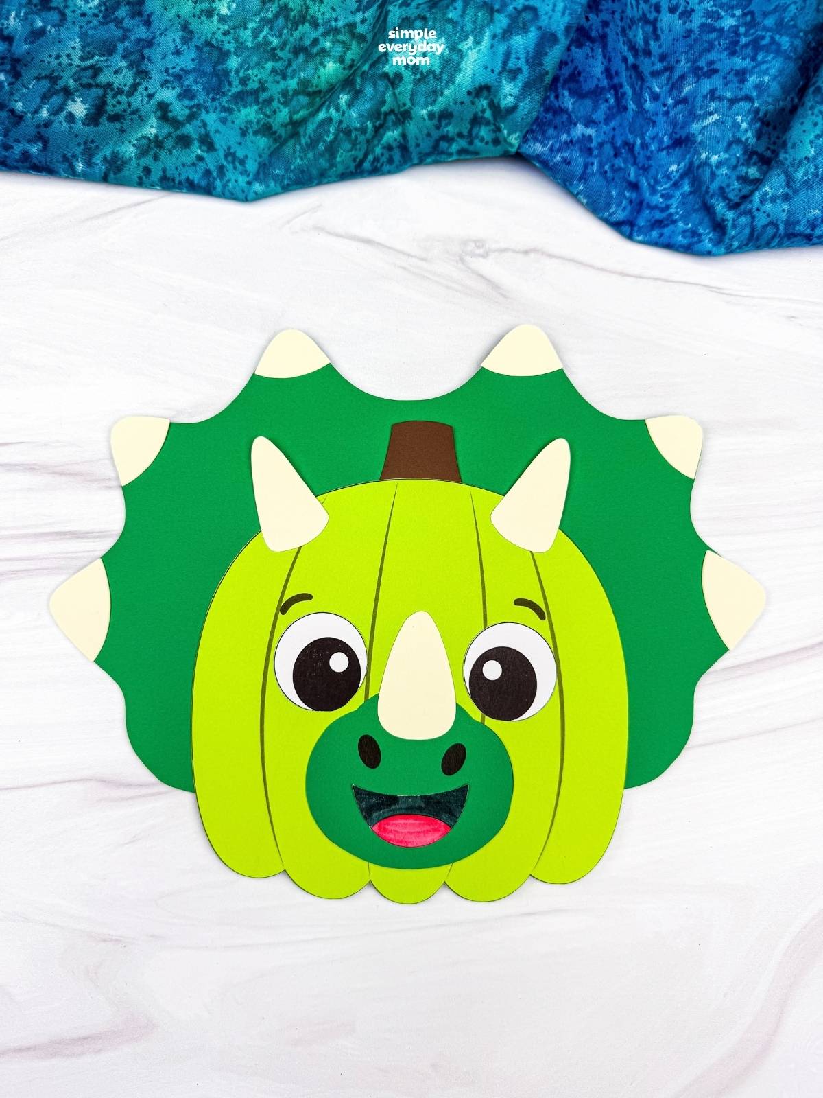 A completed craft showing a green dinosaur pumpkin disguise with horns, a smiling face, and a spiked frill.
